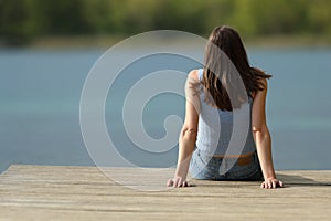 Back view of a woman sitting in a pier contemplating lake