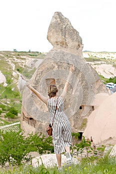 Back view woman standing with raised hands in Cappadocia, ancient cave town in background, Turkey.