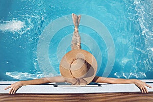 Back view of woman in straw hat relaxing in swimming pool on Tropical Resort. Exotic Paradise. Travel, Tourism and Vacations