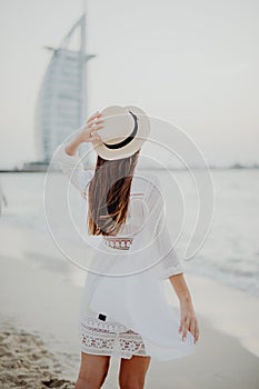 Back view of woman in straw hat walking on sandy beach eanjoying sea view