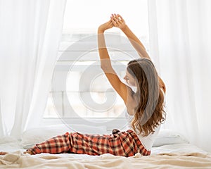 Back view of woman stretching in bed after wake up, entering new day happy and relaxing