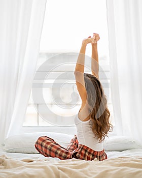 Back view of woman stretching in bed after wake up, entering new day, vertical