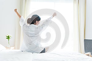 Back view of woman stretching in morning after waking up on bed near window. Holiday and Relax concept. Lazy day and Working day