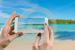 Back view of a woman taking photograph with a smart phone camera at the horizon on the beach