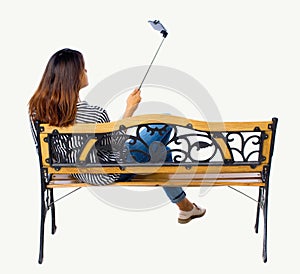 Back view of a woman to make selfie stick portrait sitting on the bench.