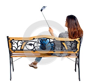 Back view of a woman to make selfie stick portrait sitting on the bench.