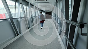 Back view of woman tourist boarding the plane walking through the gate bridge at the airport terminal. Travel concept
