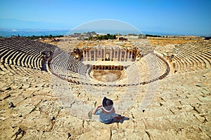 Back view of woman traveler in hat looking at amazing Amphitheater ruins in ancient Hierapolis, Pamukkale, Turkey. Grand panorama photo