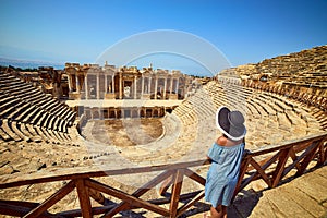 Back view of woman traveler in hat looking at amazing Amphitheater ruins in ancient Hierapolis, Pamukkale, Turkey. Grand panorama