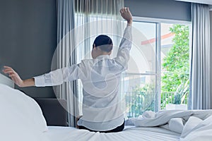 Back view of woman wake up in the morning and stretching hand on the bed