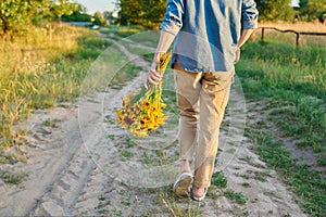 Back view, woman walking on road with bouquet of flowers, sunset light