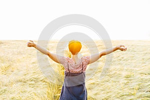 Back view woman in wheat field on sunset. Arms raised up to the sky, celebrating freedom. Positive emotions feeling life