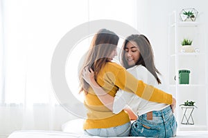 Back view of women lesbian happy couple waking up in morning, sitting on bed, stretching in cozy bedroom.