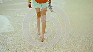 back view women's slim legs, girl walks alone sea water at sandy beach, enjoying wind, sea waves and cloudy sky
