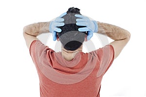 Back view of worried person with virus protection surgical face mask and gloves holding his head in panic, looking at wall.
