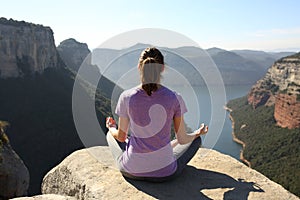 Back view of a yogi practicing yoga on a cliff