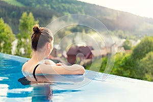 back view young adult female person enjoy relax in infinity edge luxury outdoor swimming pool looking on fog hill green