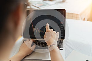 Back view, Young adult female trader, investor, businesswoman using, pointing computer laptop with financial chart graph for