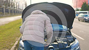 Back view of a young adult male open the hood is examining the broken engine