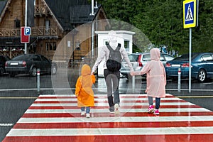 Back view of young adult mother hold daughter and son hand crossing zebra crosswalk road hiking at mountain village