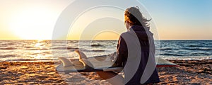 Back view young adult slim sporty female surfer girl with surfboard sitting on sand at ocean coast wave against warm