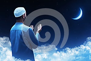 Back view of young asian muslim man with beard pray at blue night sky with stars and crescent moon