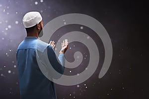 Back view of young asian muslim man with beard praying on dark backgrounds