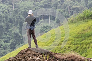 Back view of young Asian traveler man taking photo on the rock outdoors scenic mountain background. Travel lifestyle and relaxatio