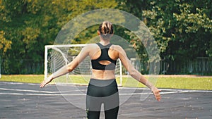 Back view on young athlete woman in sport outfit engaged in fitness on the sports field in the park.