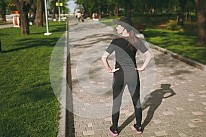 Back view Young athletic beautiful brunette girl in black uniform, cap standing, resting and looking aside before or