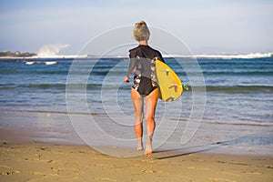 Back view of young attractive and sporty surfer girl in cool swimsuit at the beach carrying surf board into the sea running toward