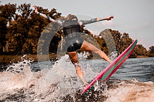 Back view of young attractive woman who stands on surf style wakeboard and jumps on wave.