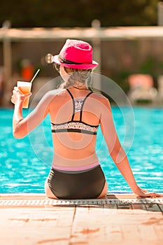 Back view of a young beautiful girl sitting at the pool side