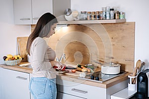 Back view of young beautiful woman is preparing lunch in her kitchen at home