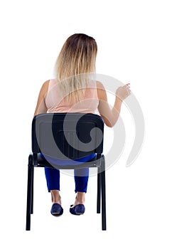 Back view of young beautiful woman sitting on chair and pointin