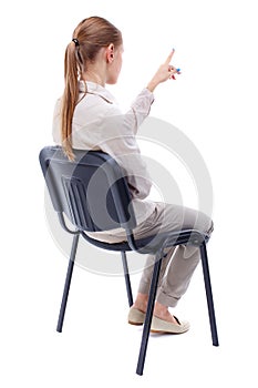 Back view of young beautiful woman sitting on chair and pointin
