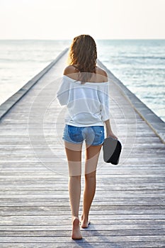 Back view of young beautiful woman walking on the pier