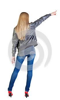 Back view of young blonde woman pointing at wall