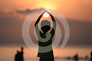 Back view of a young boy silhouette standing and doing Surya Namaskar