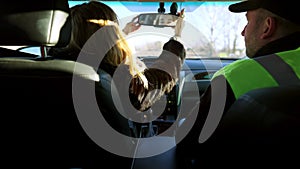 Back view of young brunette woman adjusting rear-view mirror as auto instructor talking sitting on passenger seat