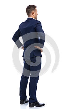 back view of young businessman in navy blue suit holding hands on hips