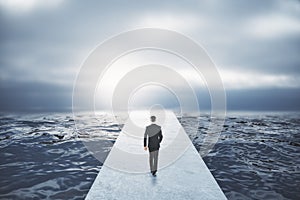 Back view of young businessman walking on pathway in dull sky.