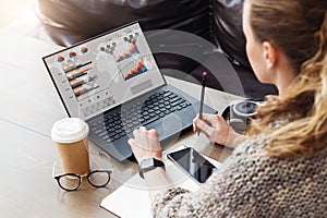 Back view. Young businesswoman sitting in office working on laptop computer with graphs, charts, diagrams on monitor