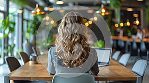 Back view of a young businesswoman using a laptop sitting at a table in the office. AI Generated.