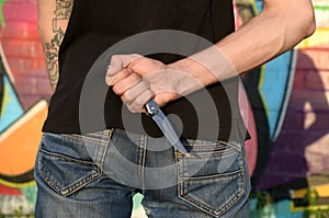 Back view of young caucasian man with knife in his hand against ghetto brick wall with graffiti paintings. Concept of criminal