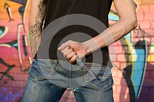 Back view of young caucasian man with knife in his hand against ghetto brick wall with graffiti paintings. Concept of criminal