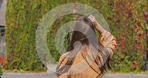 Back view of a young Caucasian woman in mustard dress with goose foot print. Wind blowing long brown hair of elegant