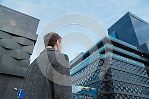 Back view of young confident man leader standing near the office building. Bottom view