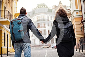 Back view of the young couple with backpacks, the whole world is ahead. A man and a girl are holding each other`s hands