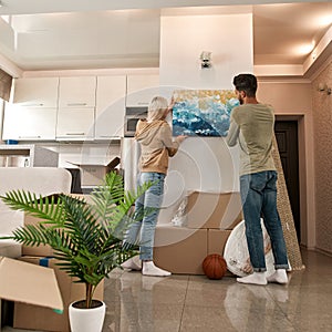 Back view of young couple hanging picture on wall